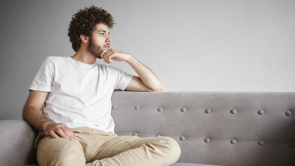 A man is sitting on the sofa, looking thoughtful.